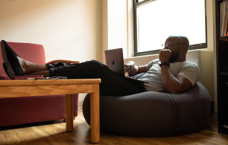 Man sitting in bean bag chair with feet up on the coffee table working from home on a laptop.